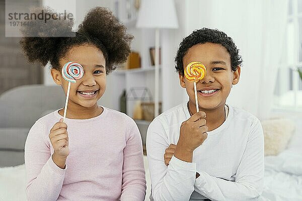 Vorderansicht zwei lächelnde Geschwister  die mit Lollipops posieren