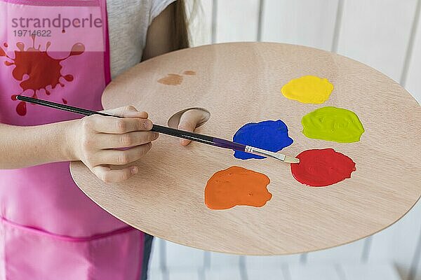 Close up Mädchen mischt Farbe mit Pinsel Holzpalette
