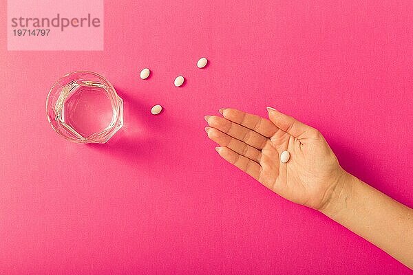 Erhöhte Ansicht weiblichen s Hand Einnahme von Medizin mit Wasserglas rosa Hintergrund