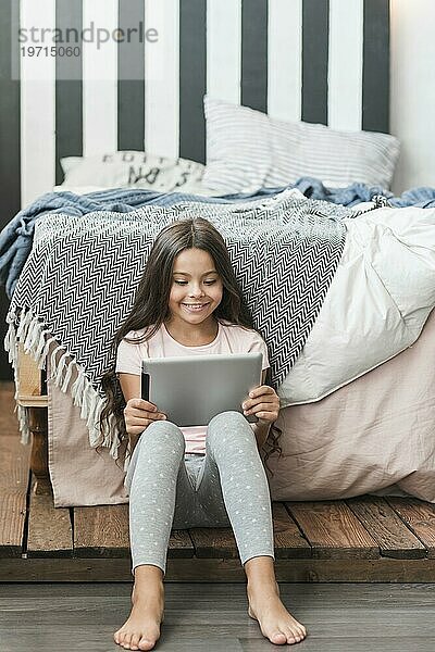 Porträt lächelnd Mädchen sitzt in der Nähe von Bett suchen digitale Tablette