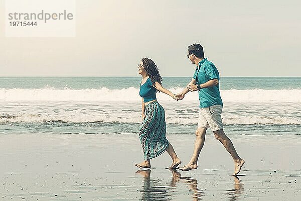 Lächelndes Paar geht barfuß am Strand entlang