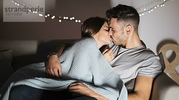 Junger Mann küsst mit Frau auf dem Sofa liegend