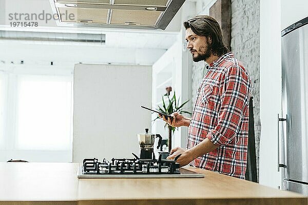 Seitenansicht junger Mann stehend Küche hält Smartphone