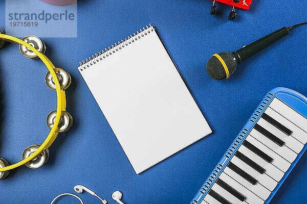 Erhöhte Ansicht leere Spirale Notizblock mit Kopfhörer Gitarre Mikrofon Klavier Tastatur Tamburin blaün Hintergrund