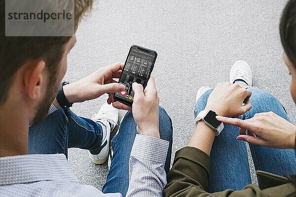 Freunde sitzen auf der Straße und verbinden ihre Smartwatch mit ihrem Mobiltelefon