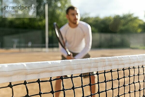 Nahaufnahme eines Netzes mit einem unscharfen Mann beim Tennisspielen