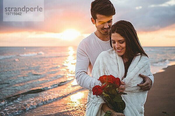 Lächelnde Paar zu Fuß Strand mit Blumenstrauß Rosen Sonnenuntergang