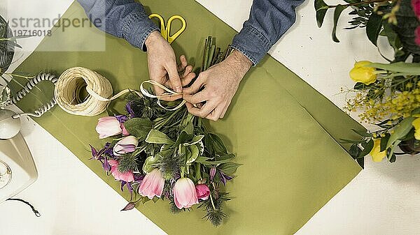 Erhöhte Ansicht männlichen Touristen binden Blumenstrauß mit String grünes Papier Schreibtisch