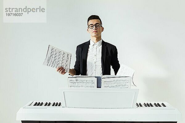 Porträt eines jungen Mannes  der ein Notenblatt hält und am Klavier steht  vor weißem Hintergrund