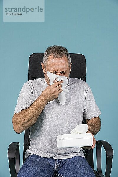 Älterer kranker Mann  der sich mit einem Taschentuch die Nase putzt