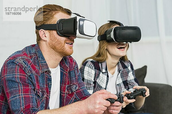 Lächelndes junges Paar  das eine Realitätsbrille trägt und sich an einem Videospiel erfreut