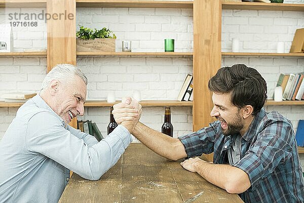 Aged Mann junger Mann mit Händen verschränkt Arm Ringen Herausforderung Tabelle Zimmer