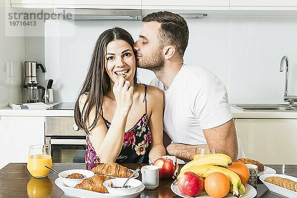 Junger Mann küsst ihre Freundin essen Kekse mit Früchten Croissant Tisch Küche