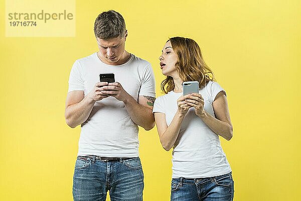Verdächtige Freundin spioniert seinen Freund SMS Handy gegen gelben Hintergrund