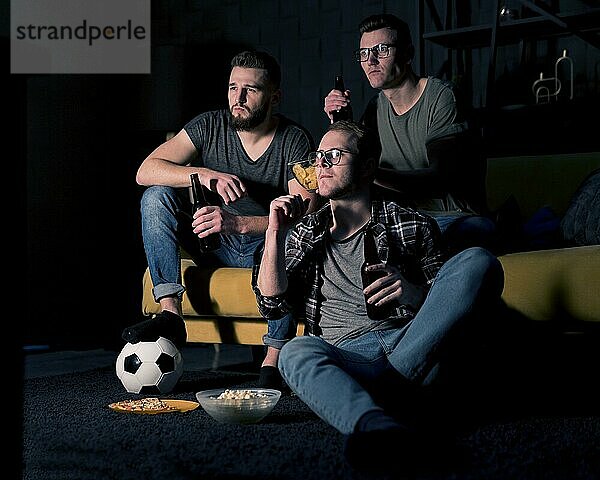 Männliche Freunde  die gemeinsam Sportfernsehen schauen  während sie Biersnacks zu sich nehmen