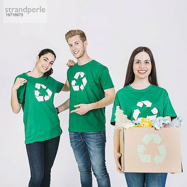 Glückliche Frau hält Karton mit recycelten Gegenständen vor ihren Freunden