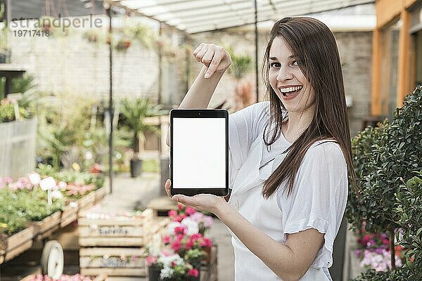 Glückliche Frau  die auf ein digitales Tablet mit leerem weißen Bildschirm zeigt