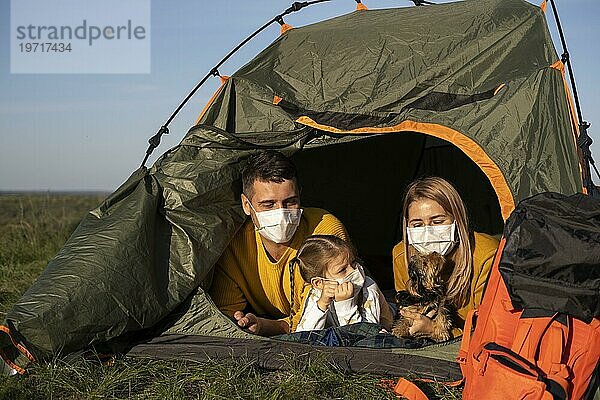 Familie mit Masken im Zelt sitzend mit ihrem Hund Vorderansicht