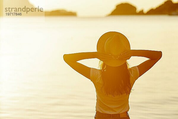 Frau mit Hut bei Sonnenuntergang am Seeufer