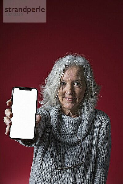 Porträt einer älteren Frau  die ein Mobiltelefon mit leerem weißen Bildschirm zeigt
