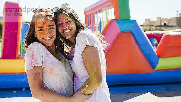 Close up glücklich junge Frauen mit Holi Farbe ihr Gesicht umarmen