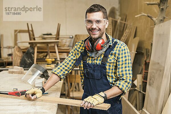 Porträt männlicher Schreiner  der eine Werkbank aus Holzbrettern hält Werkstatt