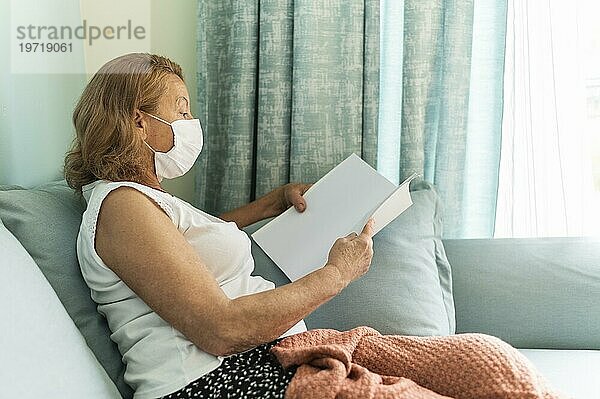 Seitenansicht ältere Frau mit medizinischer Maske zu Hause während der Pandemie  die ein Buch liest