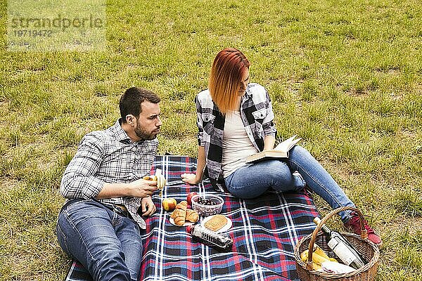 Mann ißt Banane mit Blick auf ihre Freundin lesen Buch Picknick