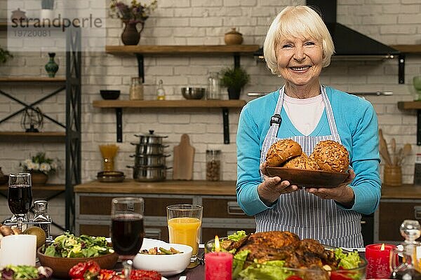 Ältere Frau hält Teller mit Brot und schaut in die Kamera
