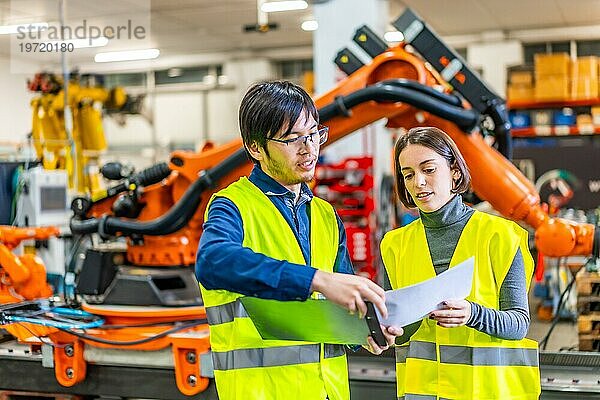Multikulturelle Ingenieure bei der Erledigung von Papierkram in einem Fließband für die Produktion von Roboterarmen