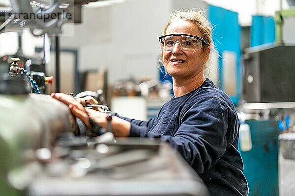 Porträt einer Fabrikarbeiterin  die im Kontrollbereich einer Metallfräsmaschine arbeitet  Industriewerk