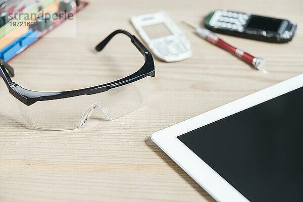 Close up digitale Tablette Schutzbrille gebrochen Handy hölzernen Hintergrund