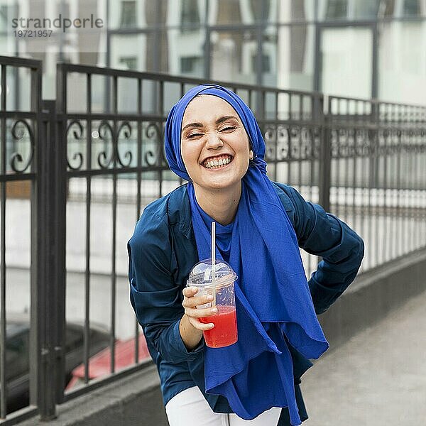 Lächelndes Mädchen mit Hidschab und Smoothie in der Hand