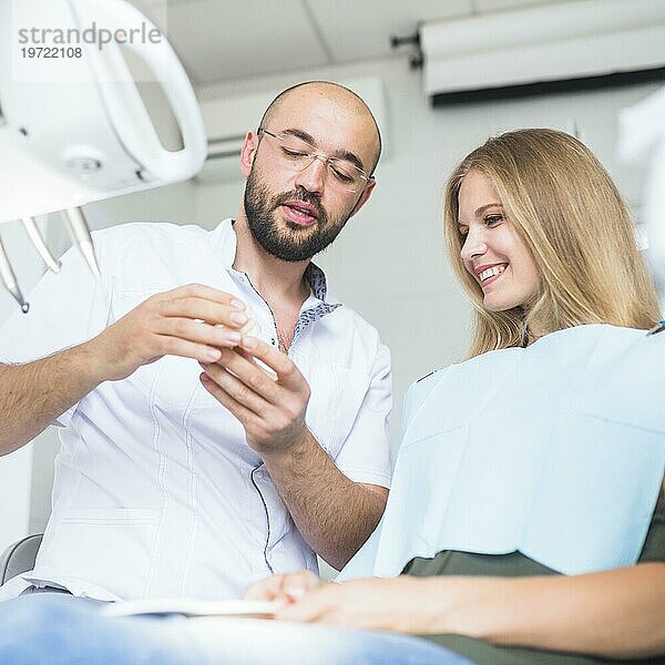 Männlicher Zahnarzt zeigt Kiefer einer glücklichen Patientin