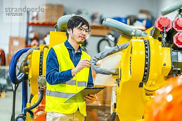 Ein junger japanischer Ingenieur kontrolliert die Produktionslinie für Roboterarme