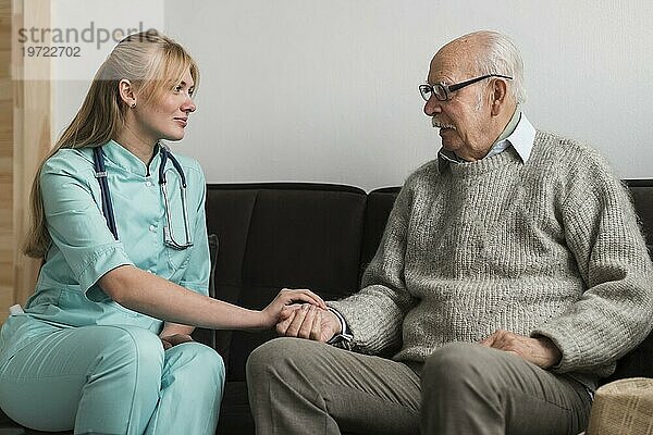 Krankenschwester hält Hand eines alten Mannes im Pflegeheim