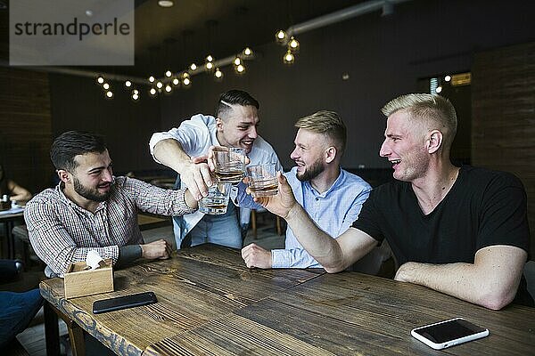Glückliche Freunde jubeln mit Whiskygläsern an der Bar