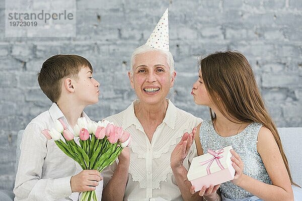 Fröhliche ältere Frau sitzt ihre Enkel mit Blumenstrauß Geschenkbox