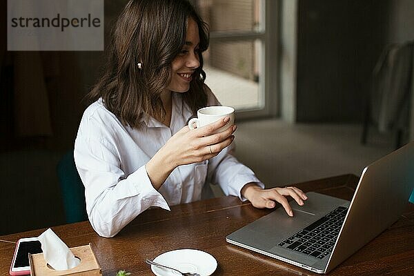 Lächelnde Frau mit Tasse Kaffee am Laptop