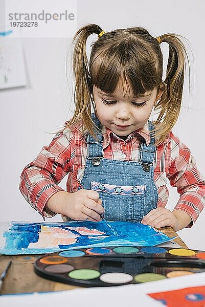 Nettes Mädchen malt mit blaür Gouache Holztisch