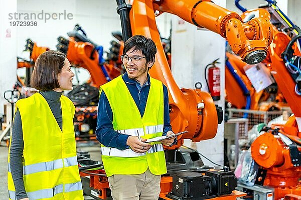 Abgelenkte multiethnische Ingenieure  die in einer Fabrik neben einem Fließband mit Roboterarmen laufen