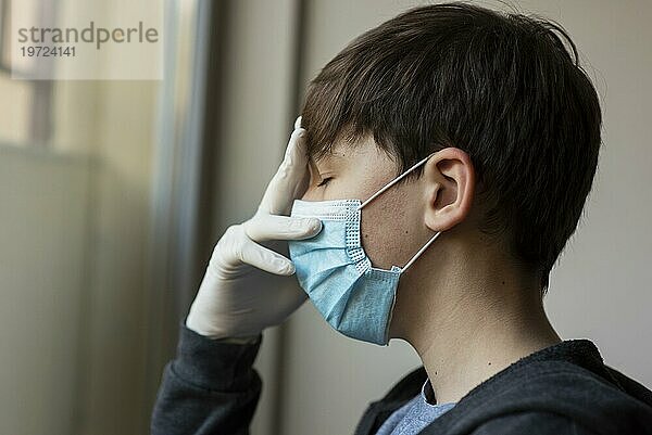 Seitenansicht Junge mit medizinischer Maske  die sein Gesicht berührt