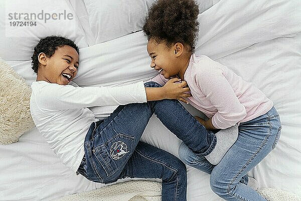 Draufsicht auf zwei Geschwister  die zusammen zu Hause im Bett spielen