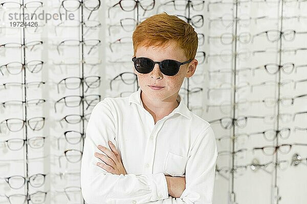 Portrait Junge mit schwarzer Brille stehend vor Brillenhintergrund