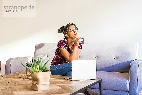 Horizontales Foto mit Kopierbereich einer nachdenklichen Frau  die zu Hause Kaffee trinkt und einen Laptop benutzt