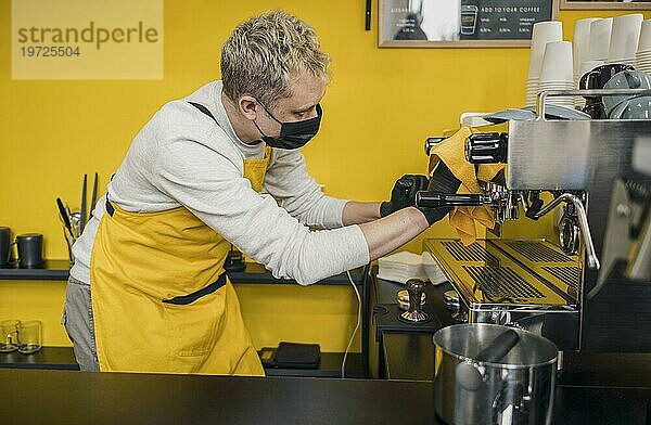 Seitenansicht männlicher Barista mit medizinischer Maske beim Reinigen der Kaffeemaschine