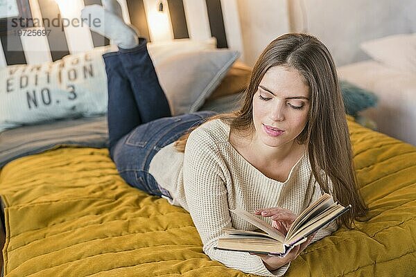 Attraktive junge Frau genießt das Lesen Buch Bett