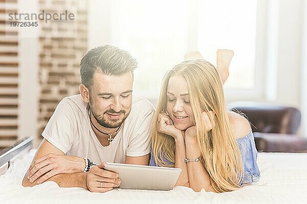 Lächelnde junge Paar liegend Bett suchen digitale Tablette Schlafzimmer