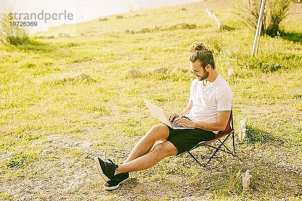 Konzentrierter Hipster arbeitet mit Laptop im Freien