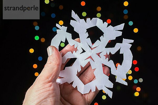 Schneeflocke geformt Papier in der Hand auf Bokeh Licht Hintergrund